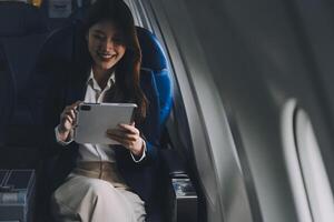 Young Asian executive excels in first class, multitasking with digital tablet, laptop and smartphone. Travel in style, work with grace. photo