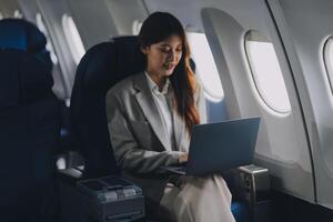 Joyful asian woman sits in the airplane and using tablet while go to travel photo