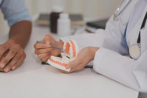 Dentist consultation - patient visit at the dental clinic office. Female dentist wearing dentures to explain teeth Recommend guidelines for orthodontics Dentist giving advice on patient's condition photo