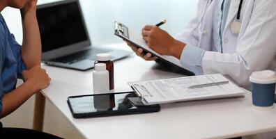 Doctor and patient sitting near each other at the wooden desk in clinic. Female physician's pointing to a records form. Medicine concept photo