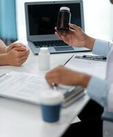 Doctor and patient sitting near each other at the wooden desk in clinic. Female physician's pointing to a records form. Medicine concept photo