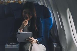 Young Asian executive excels in first class, multitasking with digital tablet, laptop and smartphone. Travel in style, work with grace. photo