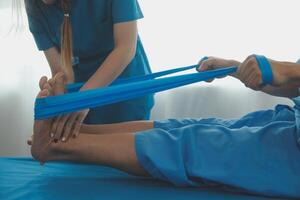 Professional orthopedist examining the little patient's leg in the clinic. Patient at the physiotherapy doing physical exercises with his therapist photo