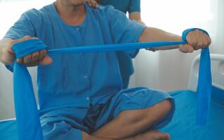 Close up hand patient doing stretching exercise with a flexible exercise band and a physical therapist hand to help in clinic room. photo
