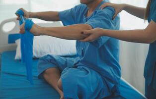 Close up hand patient doing stretching exercise with a flexible exercise band and a physical therapist hand to help in clinic room. photo