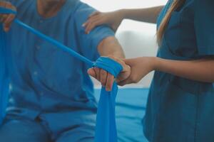 Close up hand patient doing stretching exercise with a flexible exercise band and a physical therapist hand to help in clinic room. photo