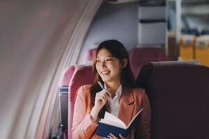 Attractive Asian female passenger of airplane sitting in comfortable seat while working laptop and tablet with mock up area using wireless connection. Travel in style, work with grace. photo