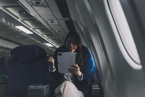 Young Asian executive excels in first class, multitasking with digital tablet, laptop and smartphone. Travel in style, work with grace. photo