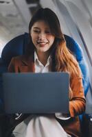 Young Asian executive excels in first class, multitasking with digital tablet, laptop and smartphone. Travel in style, work with grace. photo
