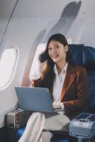 Young Asian executive excels in first class, multitasking with digital tablet, laptop and smartphone. Travel in style, work with grace. photo