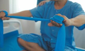 Close up hand patient doing stretching exercise with a flexible exercise band and a physical therapist hand to help in clinic room. photo