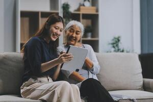 Happy grownup daughter showing content on tablet to mature mother. Two family generations women with digital computer gadget resting on couch together, watching videos, making call photo