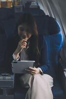 Young Asian executive excels in first class, multitasking with digital tablet, laptop and smartphone. Travel in style, work with grace. photo