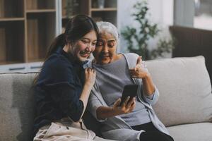 Cheerful mother and pretty teenager kid relaxing at cozy home, using mobile phone for Internet communication, resting on sofa with digital gadget, enjoying leisure, looking at camera photo