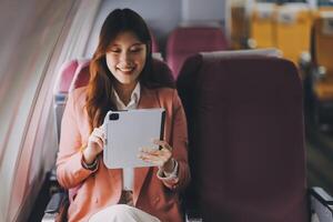 Attractive Asian female passenger of airplane sitting in comfortable seat while working laptop and tablet with mock up area using wireless connection. Travel in style, work with grace. photo