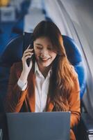 Young Asian executive excels in first class, multitasking with digital tablet, laptop and smartphone. Travel in style, work with grace. photo