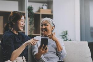 Cheerful mother and pretty teenager kid relaxing at cozy home, using mobile phone for Internet communication, resting on sofa with digital gadget, enjoying leisure, looking at camera photo