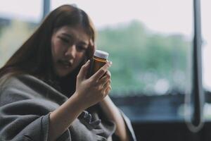 A woman with a cold with pills is treated at home chooses which drugs to take and self-medicates, checks the expiration date while sitting on the couch at home photo