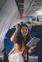 Joyful asian woman sits in the airplane and using tablet while go to travel photo