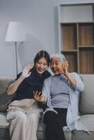 Cheerful mother and pretty teenager kid relaxing at cozy home, using mobile phone for Internet communication, resting on sofa with digital gadget, enjoying leisure, looking at camera photo