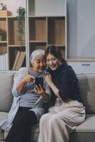 Cheerful mother and pretty teenager kid relaxing at cozy home, using mobile phone for Internet communication, resting on sofa with digital gadget, enjoying leisure, looking at camera photo
