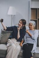Cheerful mother and pretty teenager kid relaxing at cozy home, using mobile phone for Internet communication, resting on sofa with digital gadget, enjoying leisure, looking at camera photo