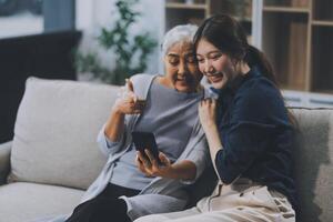 Cheerful mother and pretty teenager kid relaxing at cozy home, using mobile phone for Internet communication, resting on sofa with digital gadget, enjoying leisure, looking at camera photo