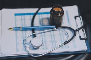 Female doctor writing in a notebook and holding a medicine bottle works at a computer while there were many medicine bottles on the table while sitting at a work desk photo