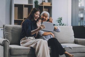 Happy grownup daughter showing content on tablet to mature mother. Two family generations women with digital computer gadget resting on couch together, watching videos, making call photo