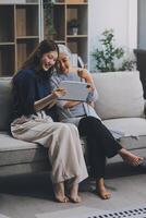 Happy grownup daughter showing content on tablet to mature mother. Two family generations women with digital computer gadget resting on couch together, watching videos, making call photo