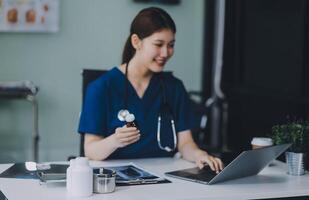 Female doctor writing in a notebook and holding a medicine bottle works at a computer while there were many medicine bottles on the table while sitting at a work desk photo