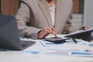 Business woman using calculator and writing make note with calculate. Woman working at office with laptop and documents on his desk photo