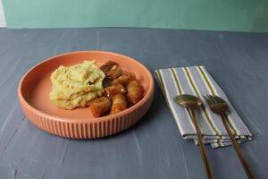 Served lunch mashed potatoes, sausages with tomato sauce, fork, spoon on napkin on a gray background. Side view photo