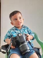 a toddler boy with an expression looking for inspiration while holding a DSLR camera photo