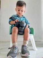 a boy sitting in a chair fiddling with a photography camera photo