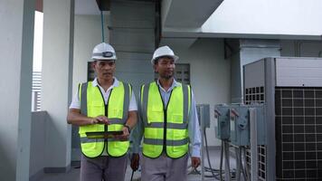 Two engineer men in safety vests are looking at a tablet. They are wearing hard hats and safety vests video