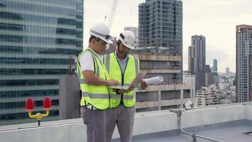 Two Engineer men are standing on a roof, one of them is writing on a laptop. The other man is looking at the laptop. Scene is serious and focused video