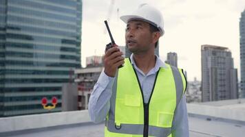 Engineer man wearing a yellow safety vest is walking on a rooftop. The man is carrying a red and white object in his hand video