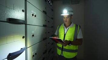 Engineer man in a yellow vest is looking at a computer screen. He is wearing a hard hat and is holding a tablet video
