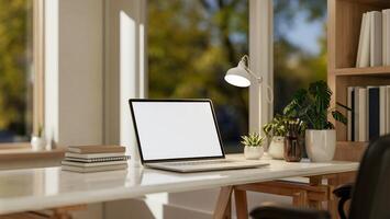 A laptop computer mockup and accessories on a white table by the window in a minimalist room. photo