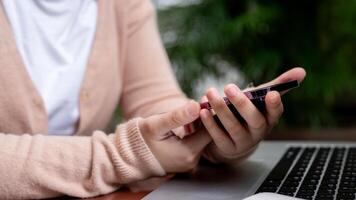 A close-up image of a woman is using her smartphone while working remotely at a table in a garden. photo