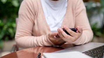 A cropped image of a woman using her smartphone while working remotely at a table outdoors. photo