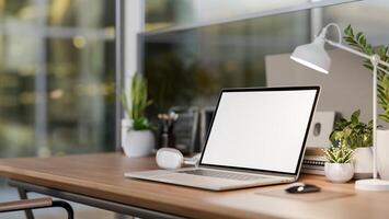 A laptop computer, a table lamp, and decorative plants on a wooden table in a modern office. photo
