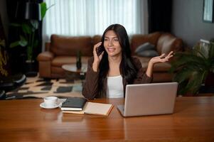 A confident Asian businesswoman is talking on the phone with a client at a desk in her office. photo