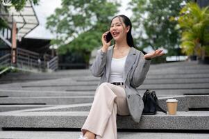 A confident Asian businesswoman is talking on the phone while sitting on the stairs outdoors. photo