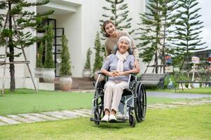 A lovely Asian granddaughter and a happy retired grandma in a wheelchair are in their home backyard. photo