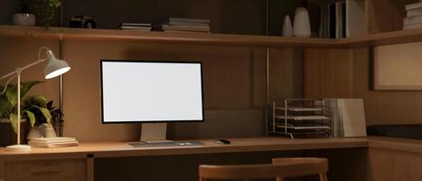 A computer mockup on a wooden table, illuminated by a table lamp in a home office workspace at night photo