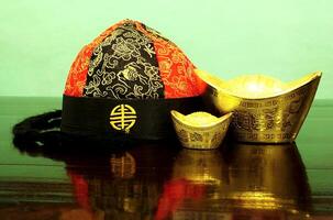 Chinese gold ingots and cheongsam hat on wooden table background. Chinese New Year concept image for good luck, wealth and prosperity. photo
