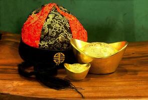 Chinese gold ingots and cheongsam hat on wooden table background. Chinese New Year concept image for good luck, wealth and prosperity. photo