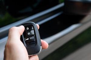 Man holding a car remote control and is pressing the car door lock button. Close up push the car door lock button on the modern car remote. photo